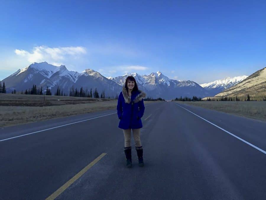 girl standing in front of rocky mountains wearing winter jacket in canada