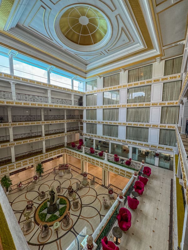Interior of a multi-level atrium with elegant balconies, a skylight, and a seating area with red chairs on the ground floor, perfect for those looking for things to do in Kandy