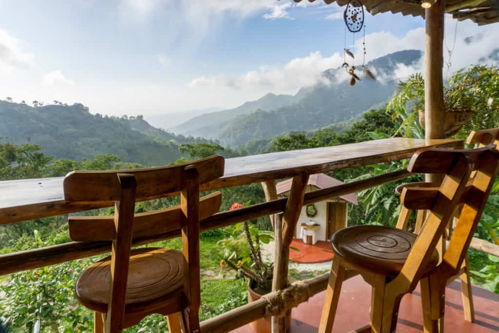 two empty wooden chairs by bench overlooking a beautiful landscape in minca colombia. in the background clouds are rolling over lush green hills.