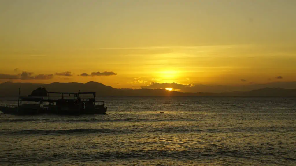 boats in ocean with an orange sunset and mountains in backdrop