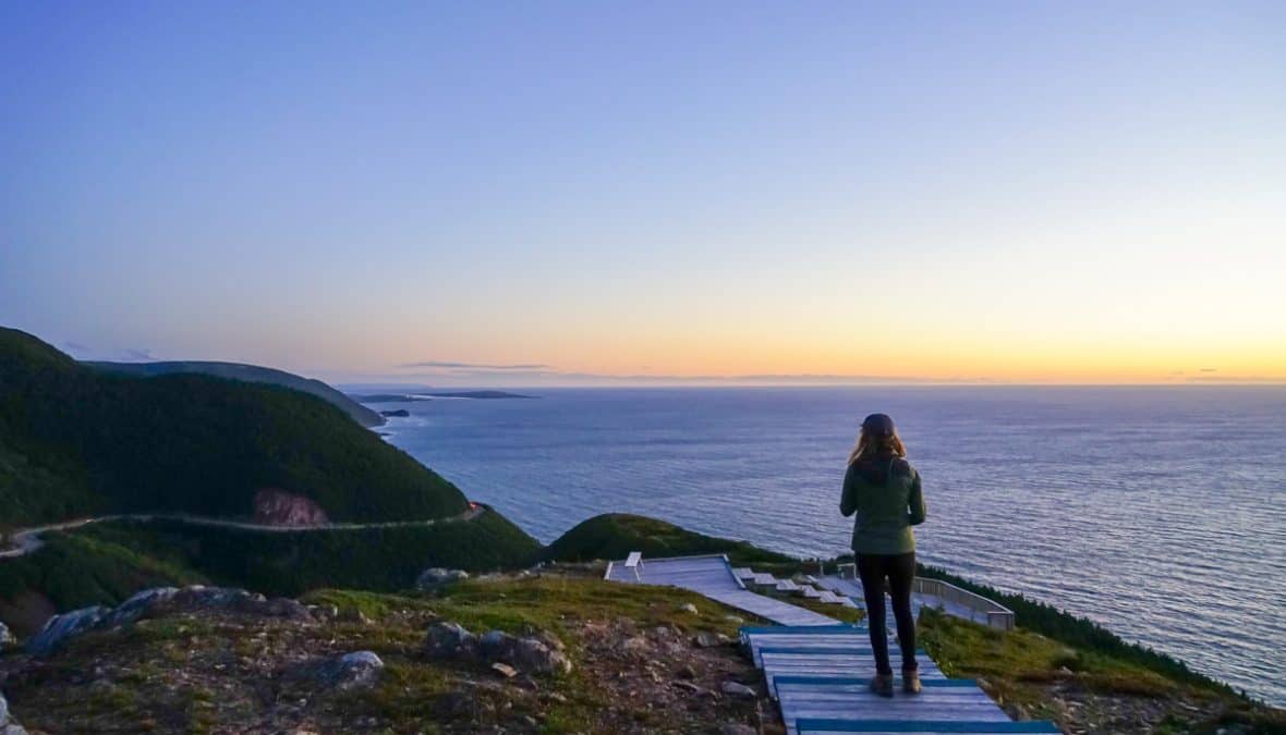 lora hiking in cape breton nova scotia during sunset. she is on a walkway looking over the ocean.