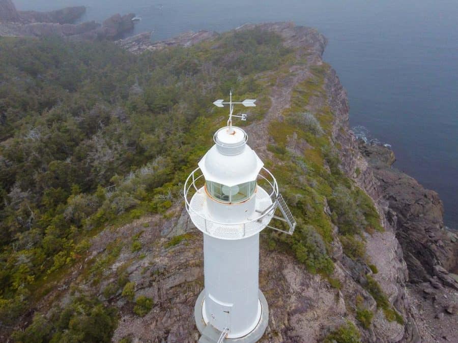 drone shot of white lighthouse on rigged cliff 