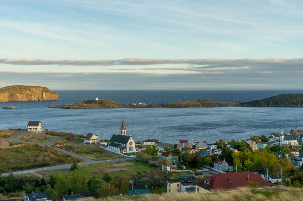 view of the town of trinity from Gun Hill Trail. colorful houses and church dot the landscape in front of the ocean.