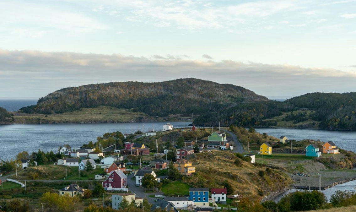 colorful houses in trinity newfoundland. in the background is the ocean and rolling hills.