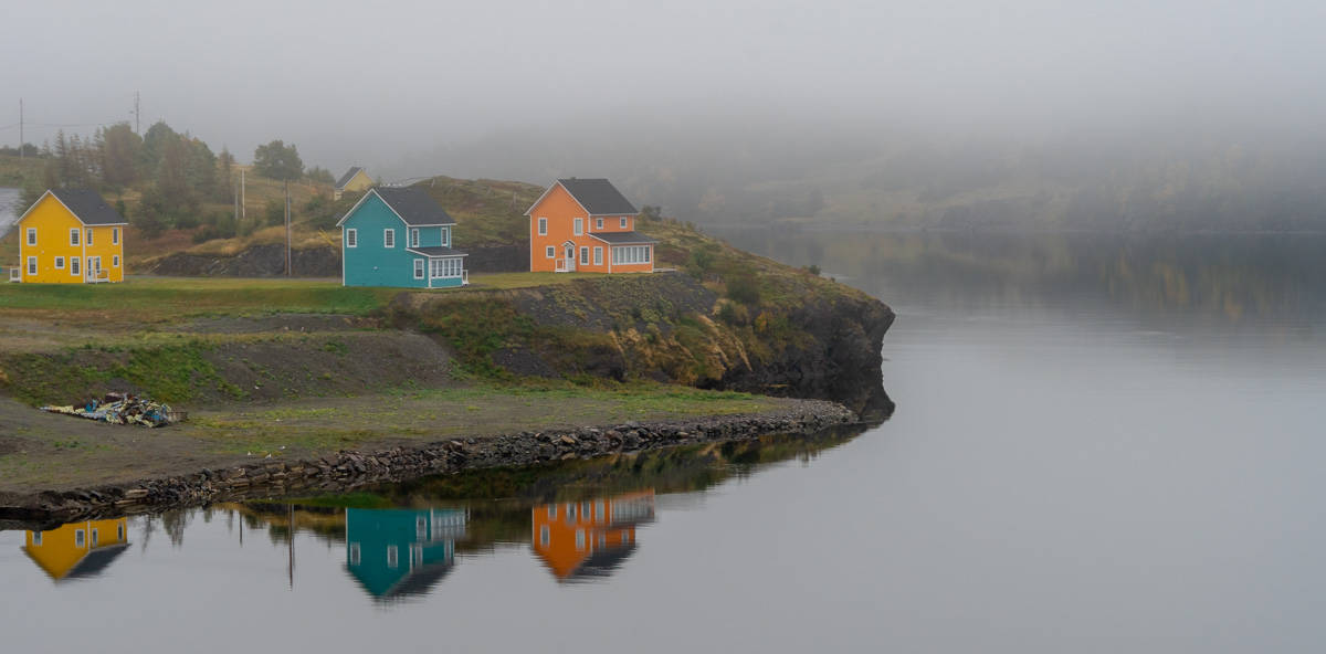 a yellow, blue, and orange house reflect in a lake