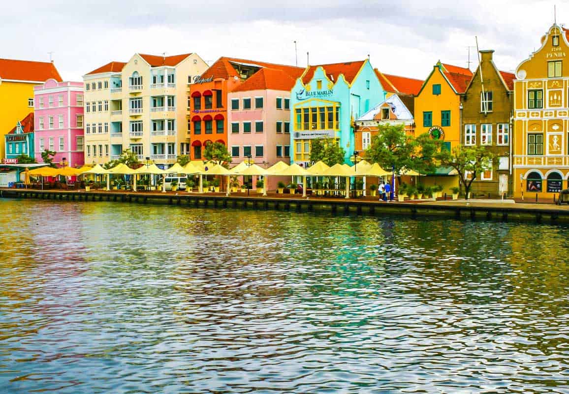 colorful houses in curacao lined on the street next to the sea.