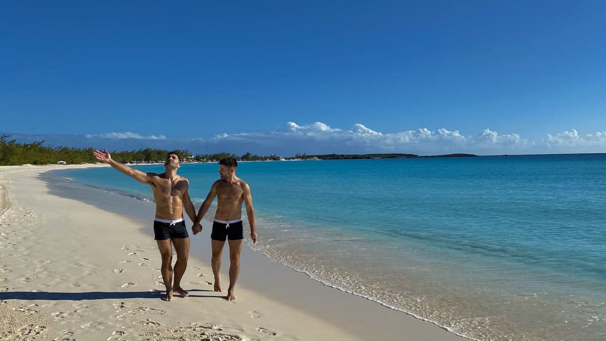 two men walking holding hands on a beach in puerto rico next to. theturquoise ocean