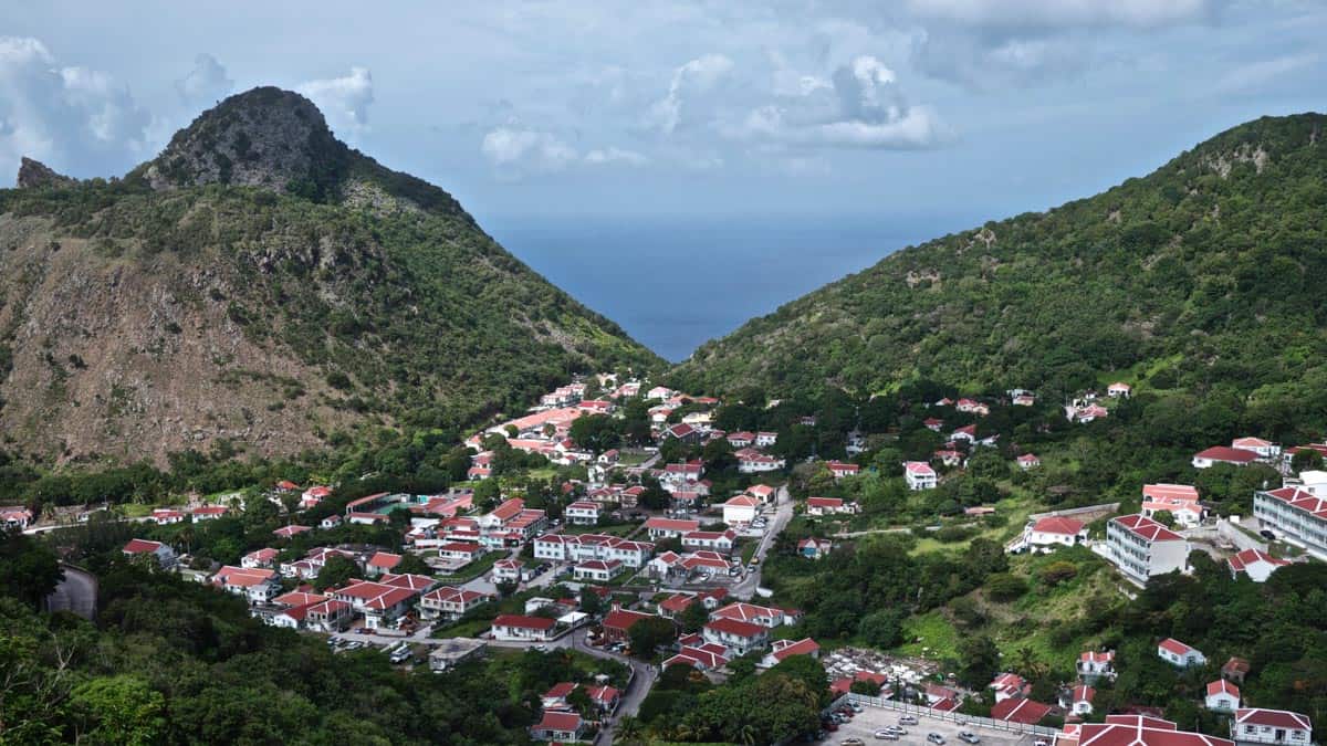 wide panoramic photo of a town on the island of saba with rolling green hills and blue sky behind it.