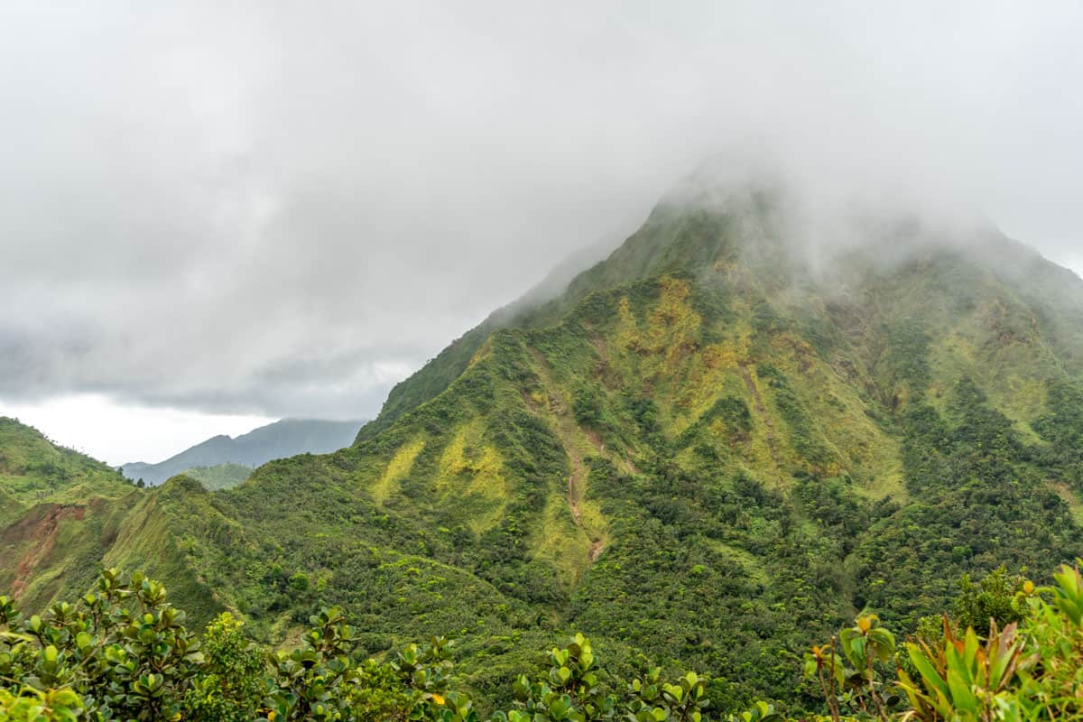 clouds rolling over the mountains in dominica. the mountains are covered in lush green vegetation.