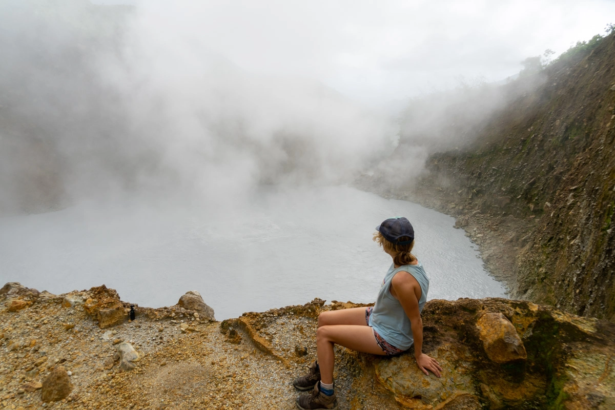 lora sitting on ledge of boiling lake dominica while steam comes out