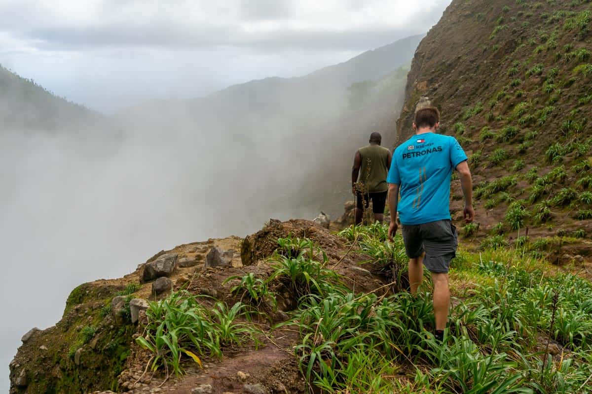 two men hiking in on the boiling lake trail in dominica. you can see the steam coming up from the lake as they walk towards it.