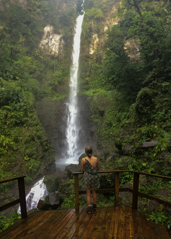 lora on viewing platform looking up at middleham falls come down through the lush jungle vegetation while hiking in dominica