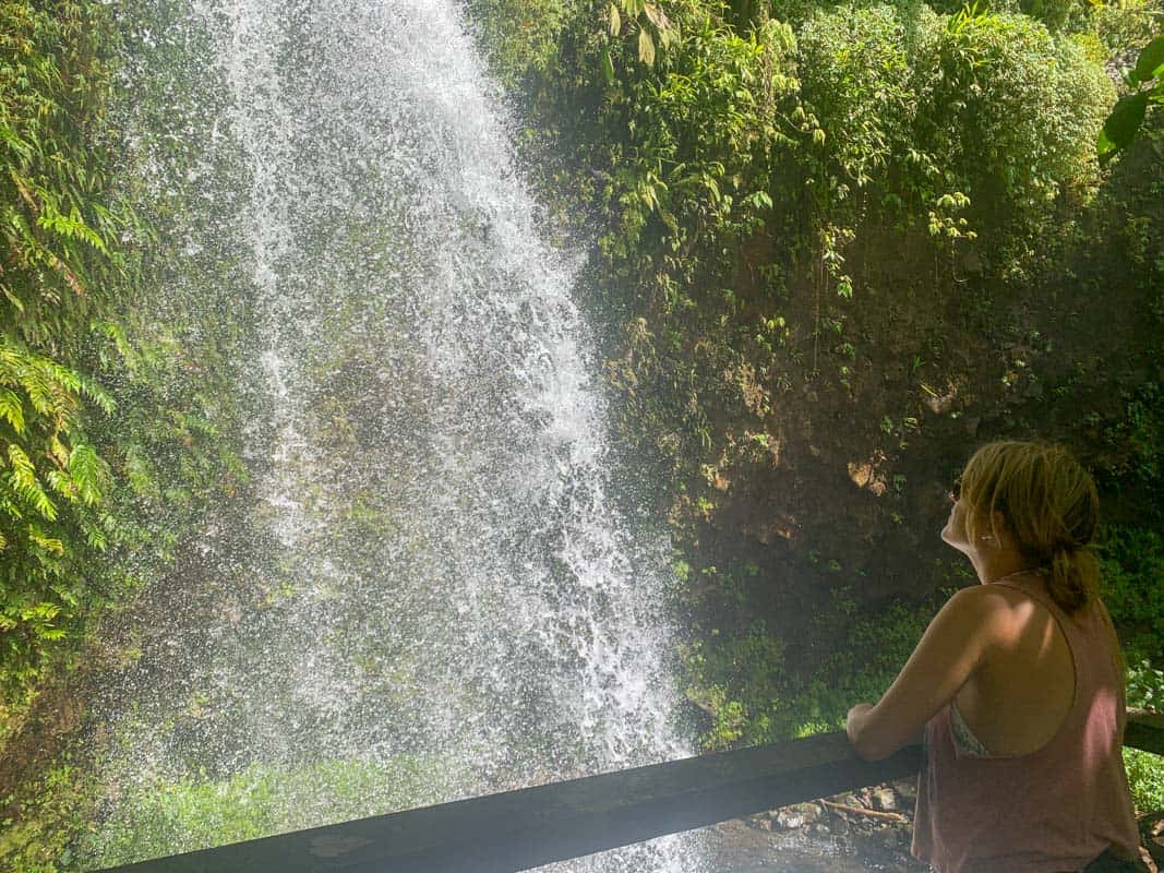 lora staniding next to railing looking up at salton waterfalls in dominica