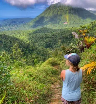 lora on boiling lake hike in dominica. she is looking at a volcano covered in lush vegetation.