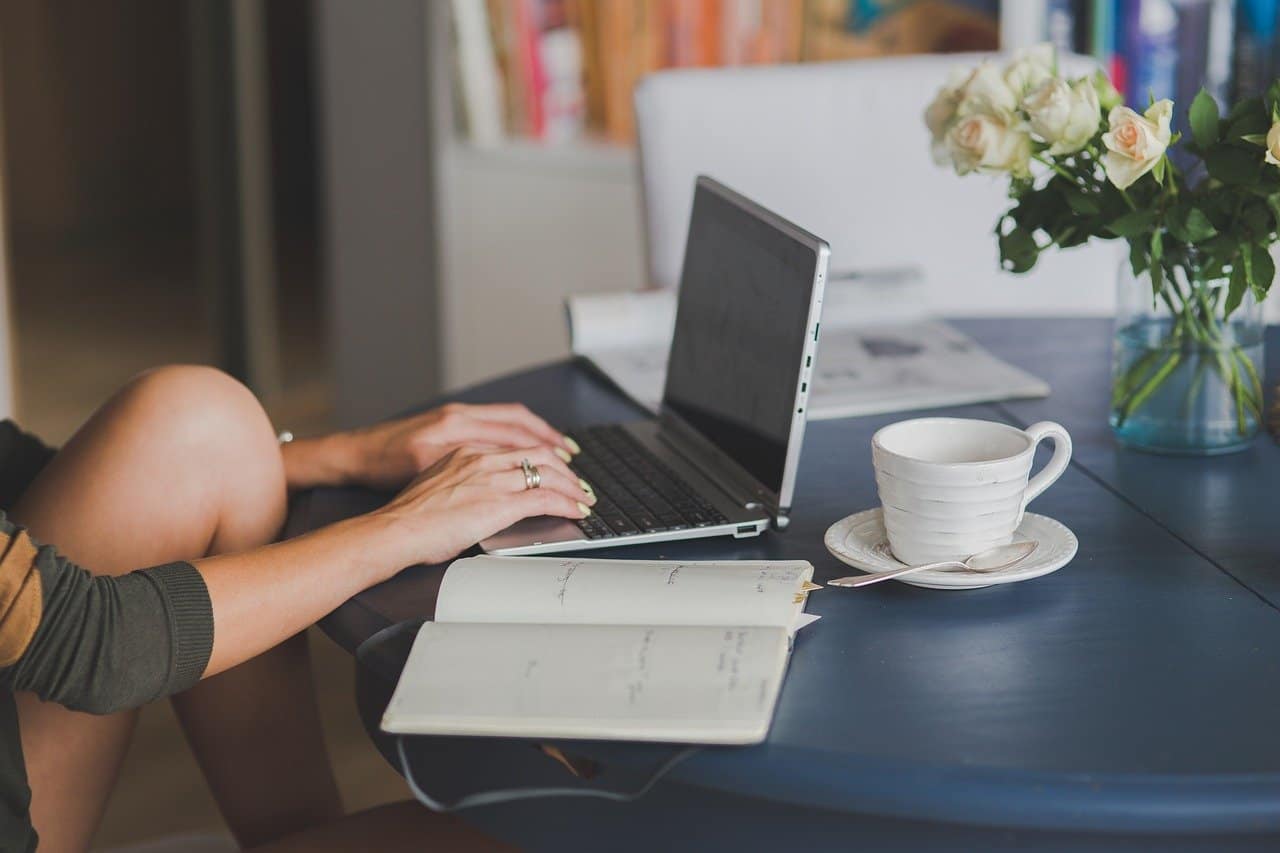 A woman sitting at a table with a laptop and flowers, taking part in a travel blogging course.