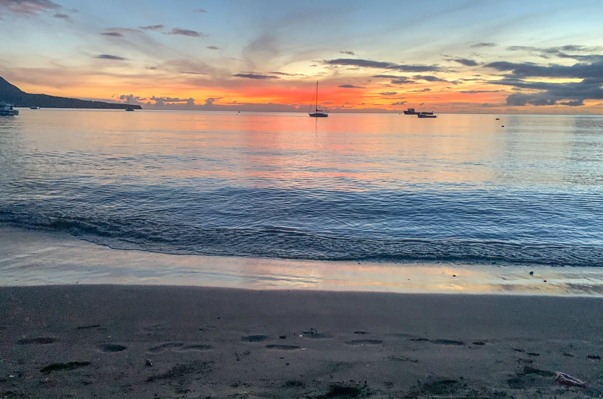 pink and orange sunset over boats in the ocean from purple turtle beach in dominica