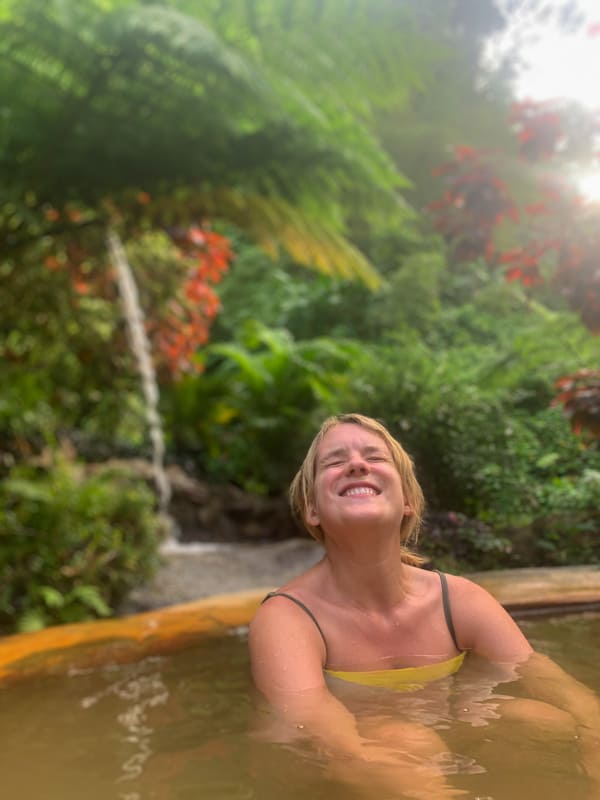 lora smiling while sitting in a hot spring in dominica with plants behind her