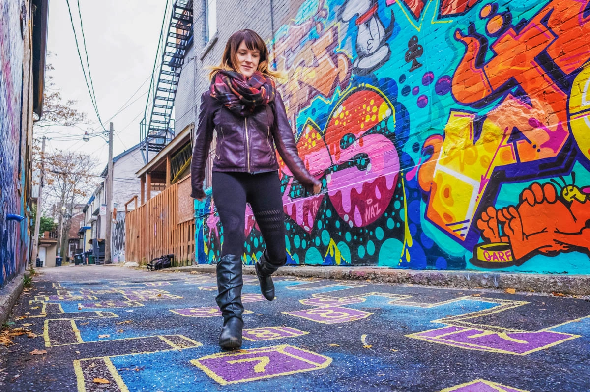 A woman walking down an alley in Toronto covered in graffiti during fall.