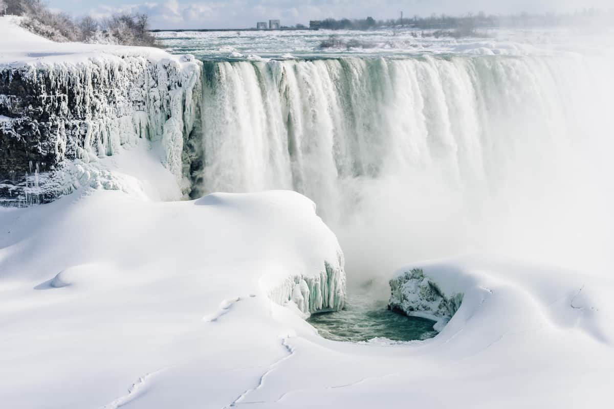 niagara falls frozen in winter. steam is coming from the base of the falls.
