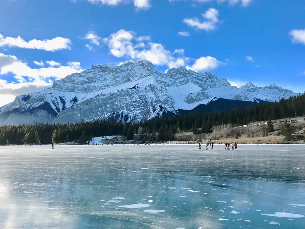 skaters on frozen lake by mountain canada