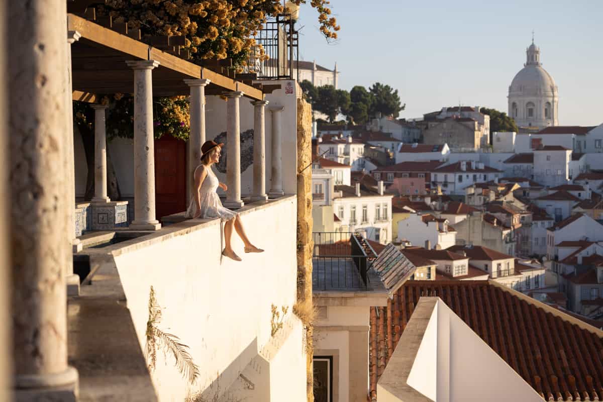 A woman is sitting on a balcony overlooking the city of lisbon.