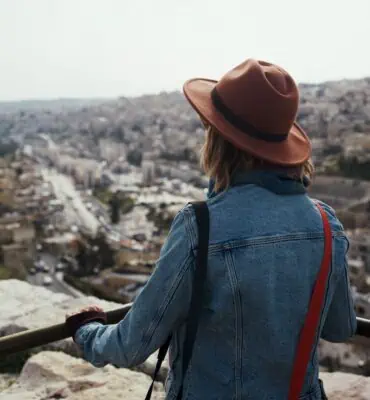 A woman in a hat looking out over the city of jerusalem.