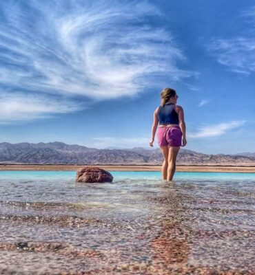 lora standing by a turquoise lagoon in dahab egypt. she is looking out into the distance.