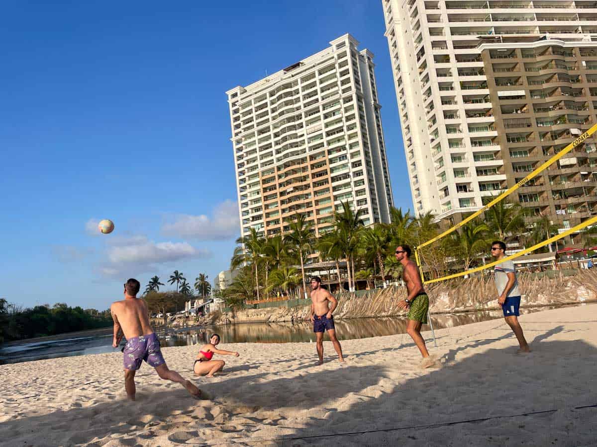 A group of people playing volleyball on the beach in front of tall buildings, 