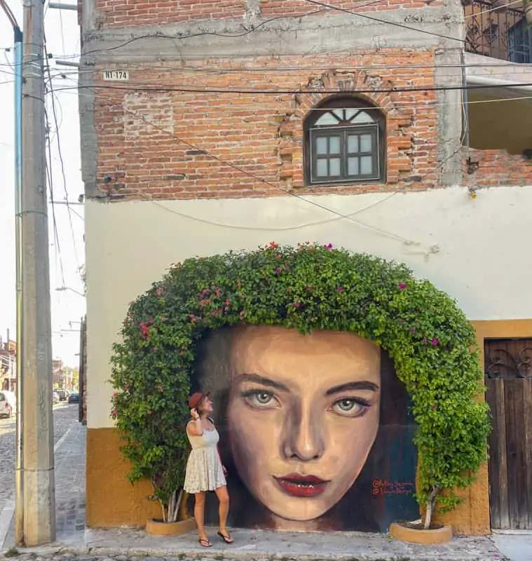 A woman is standing in front of a mural of a woman's face.