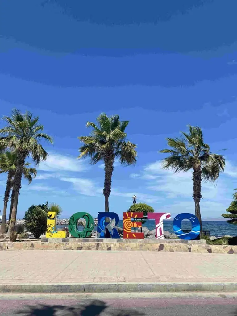 A sign for Loreto standing on a picturesque walkway overlooking the beach, inviting visitors to explore this coastal cheap beach town in Mexico