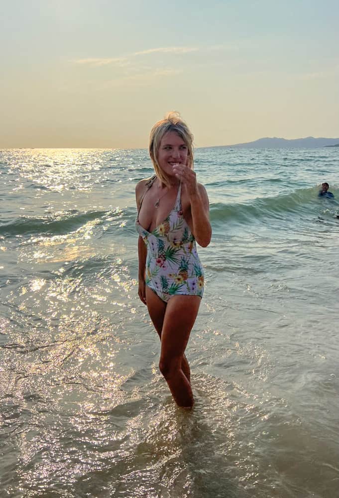 lora standing in the ocean with waves crashing behind her at sunset in puerto vallarta, one of the cheapest places to live in mexico on the beach