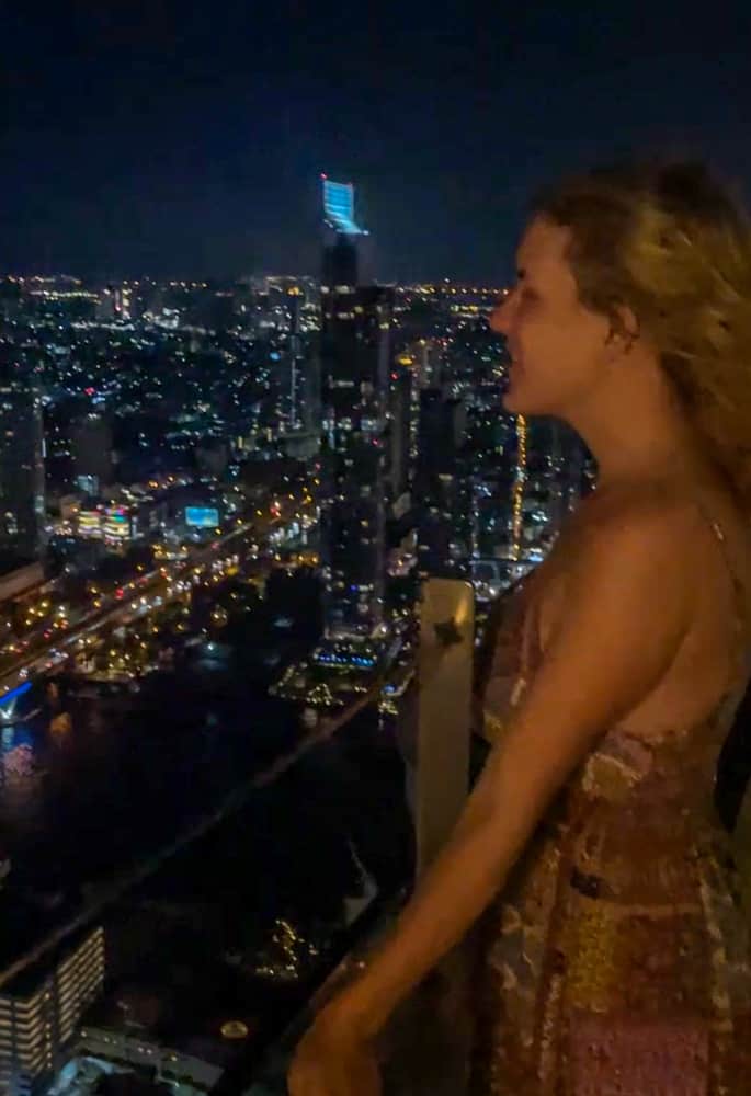 A woman peacefully admiring the cityscape of Bangkok at night.