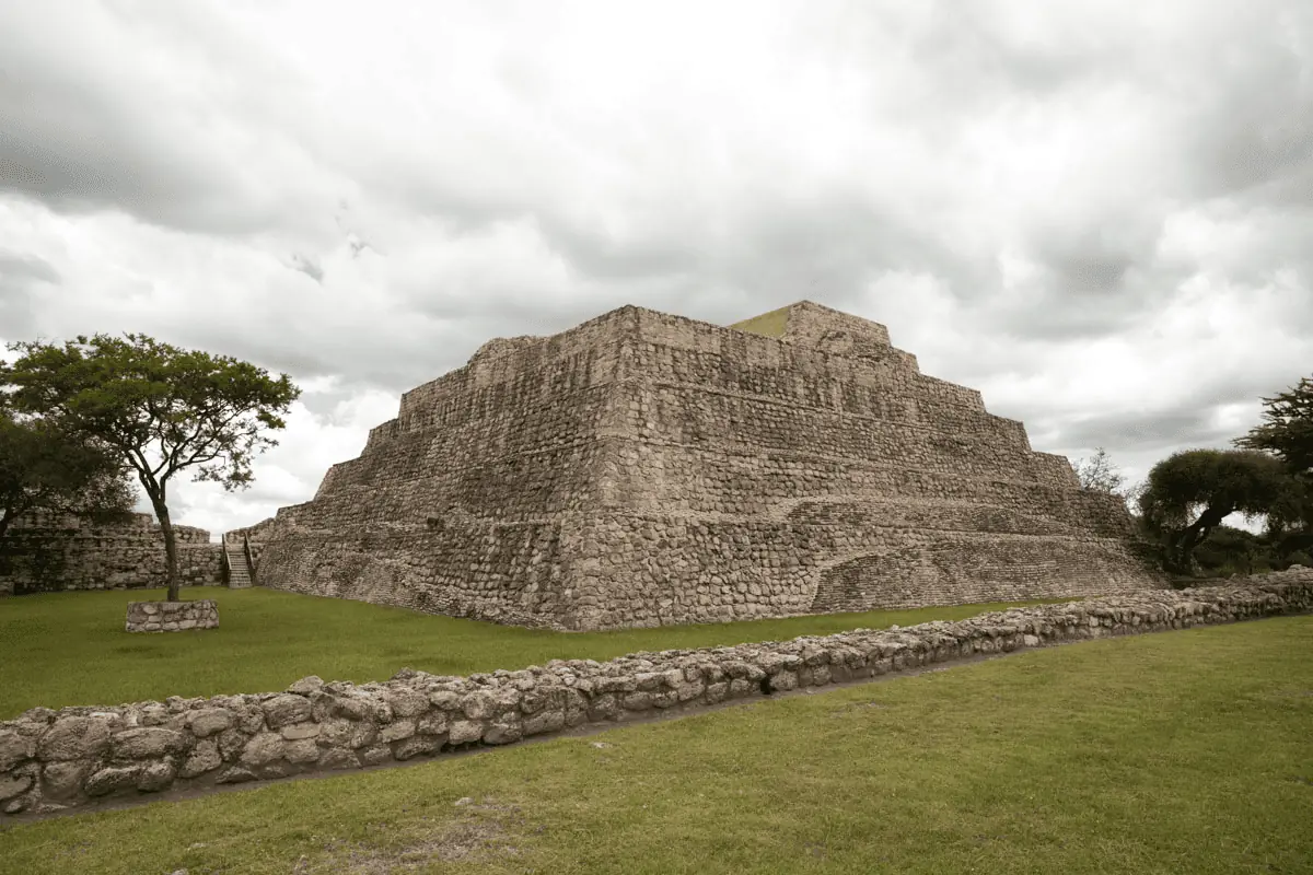 A pyramid in a grassy area with a cloudy sky.