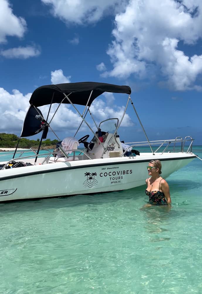 lora in turquoise water walking past a white boat that says coco vibes tours