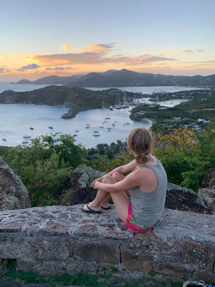 lora looking out from shirley heights viewpoint. behind her are sailboats, rolling hills, and a pink sunset.