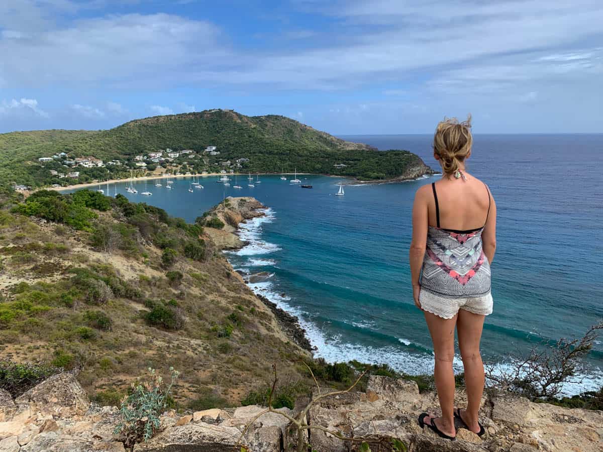lora looking out at ocean on a hiking trail in antigua. sailboats are in the distance.