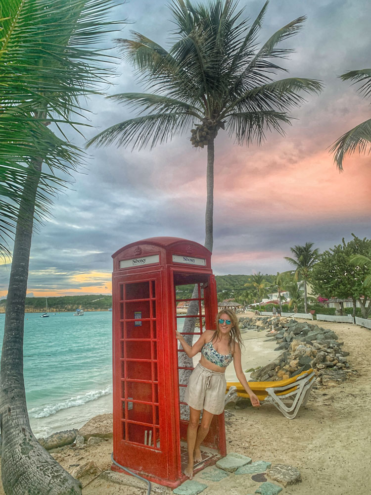 lora next to a red telephone booth on a beach in antigua