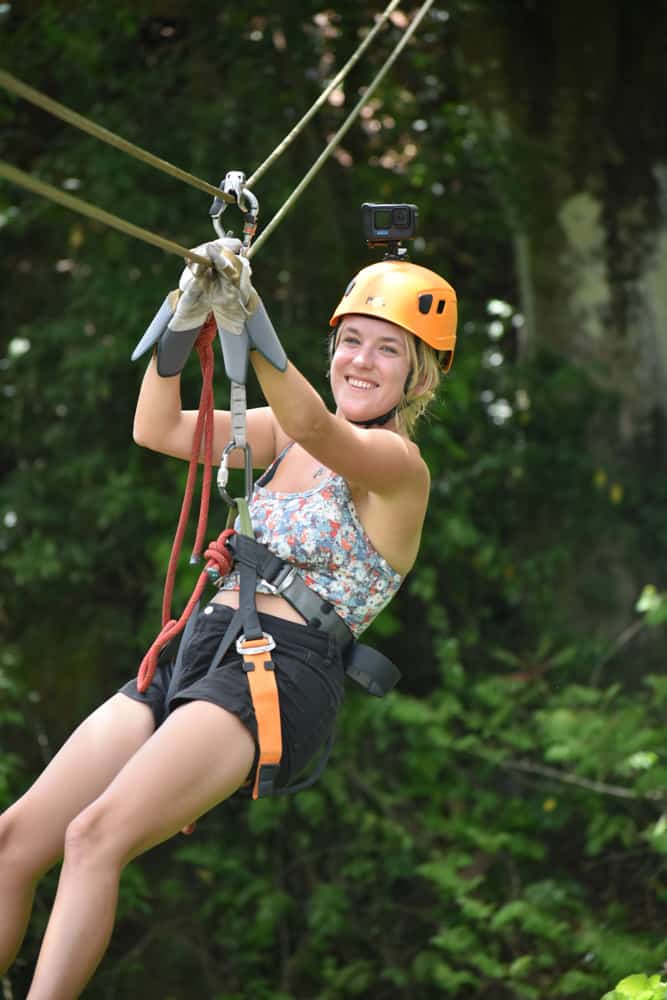 lora on a zipline smiling with green rainforest in background
