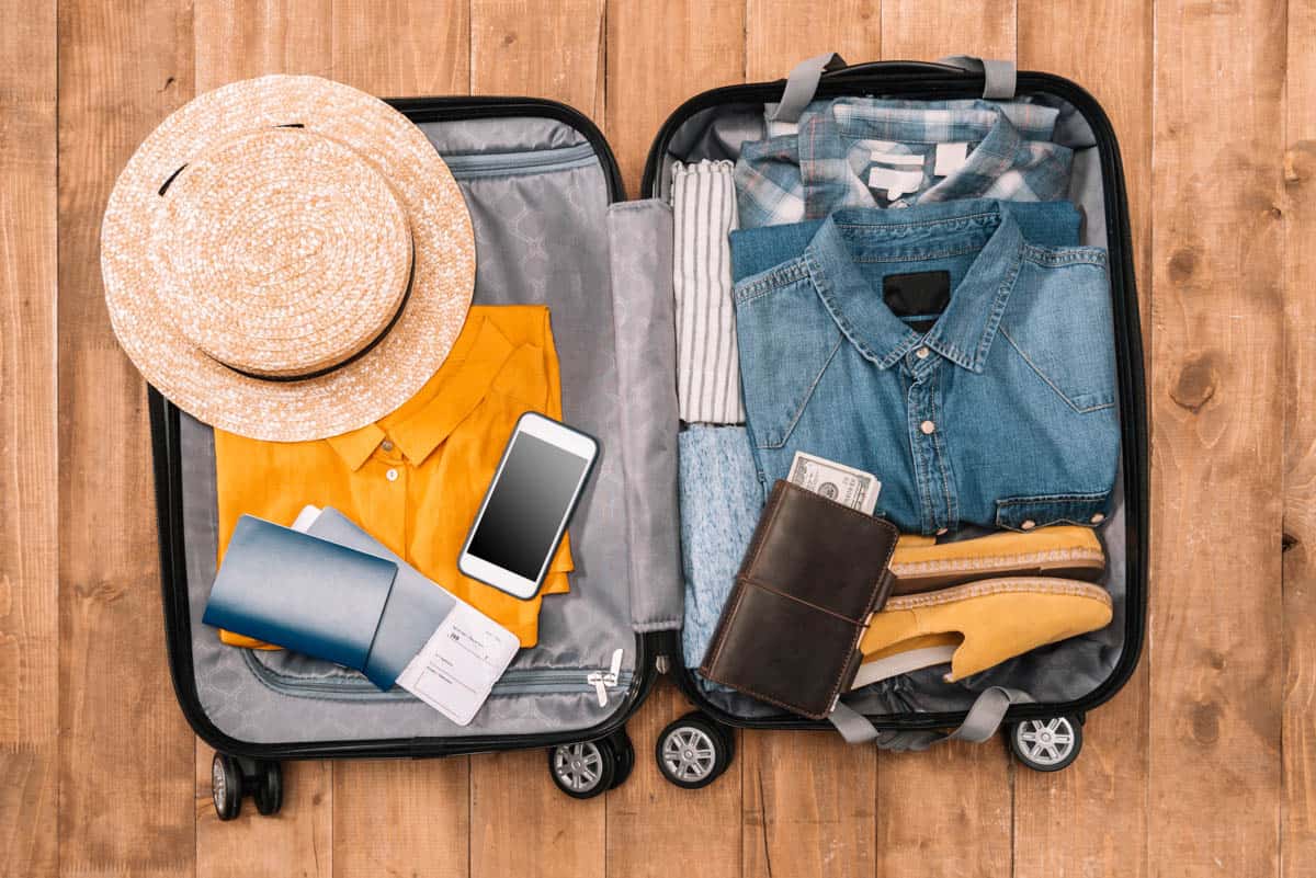 suitcase being packed with clothes, phone, and sunhat