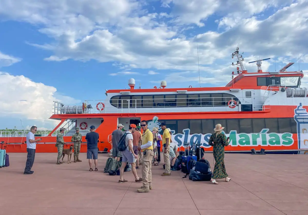 A group of people standing next to a ferry with luggage.