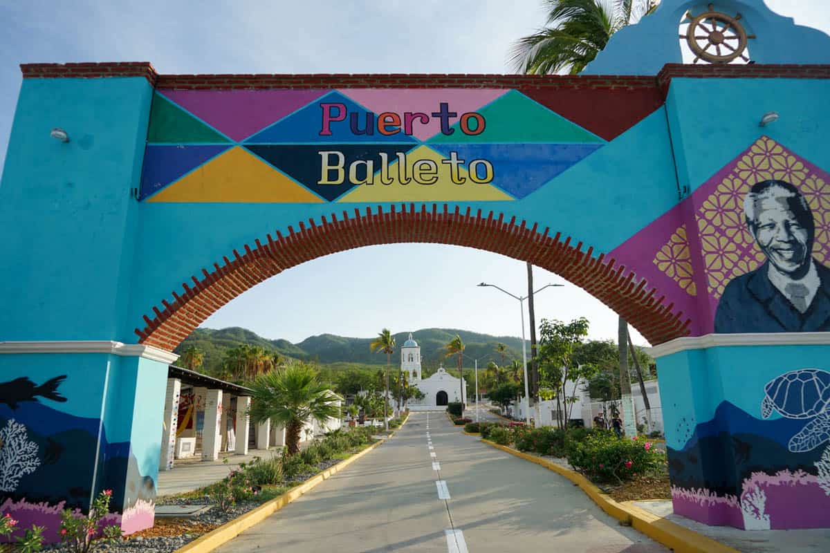colorful sign that reads puerto baleto with road leading to white church