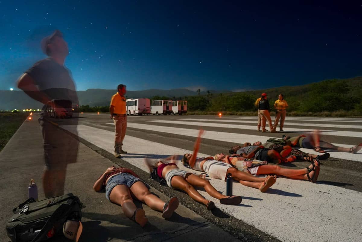 A group of people laying on an airplane runway at night stargazing at the sky