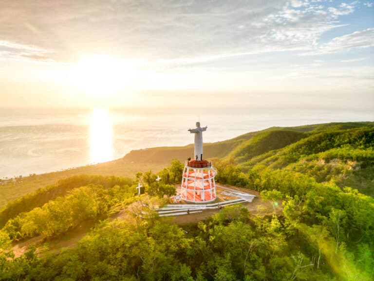 aerial shot of christ the redeemer statue looking over sunset rising on the ocean in islas marias mexico