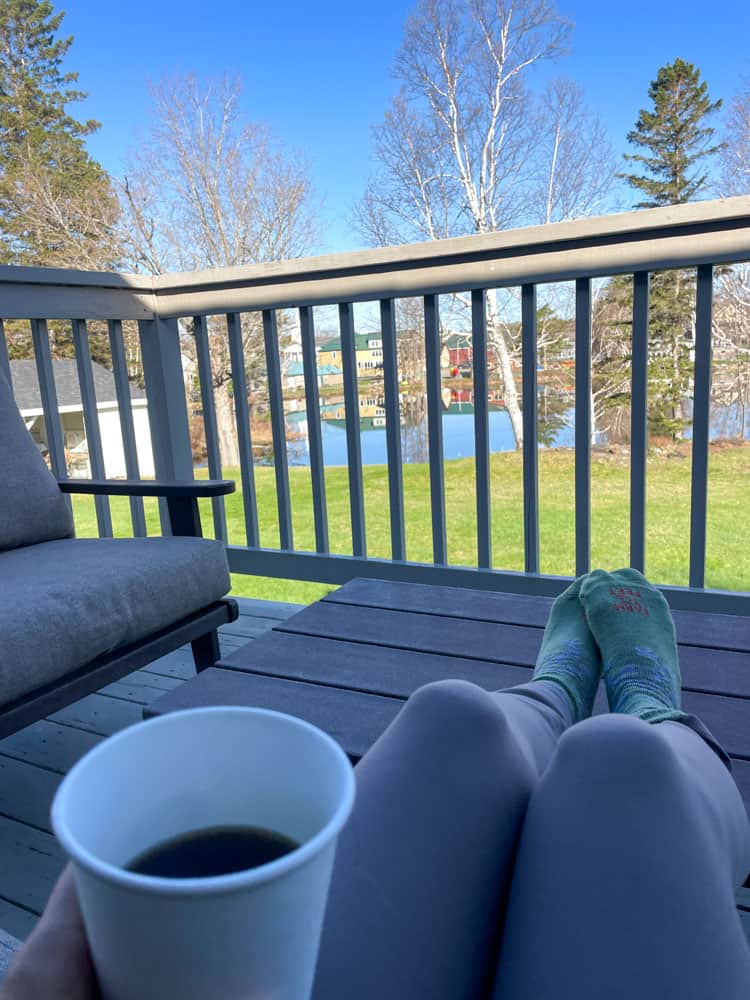 lora with feet up on table on deck drinking coffee at the rangeley inn