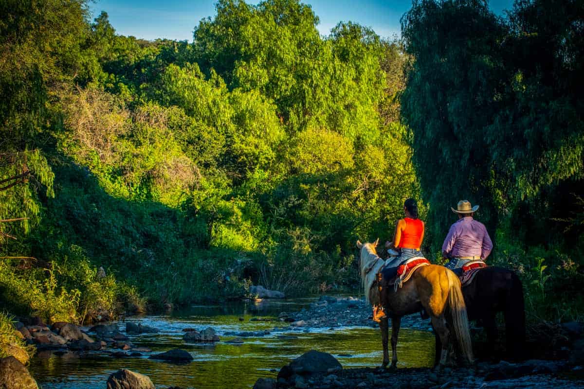 Two cowboys riding horses through a stream.