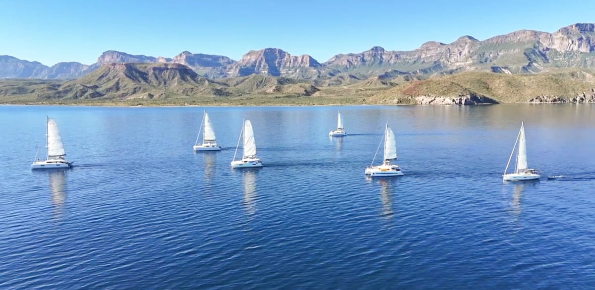 A group of sailboats in a body of water with mountains in the background.