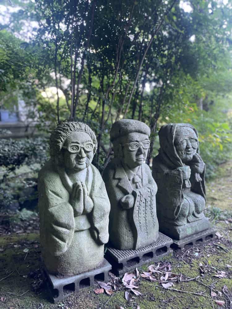 Three stone statues in a garden.
