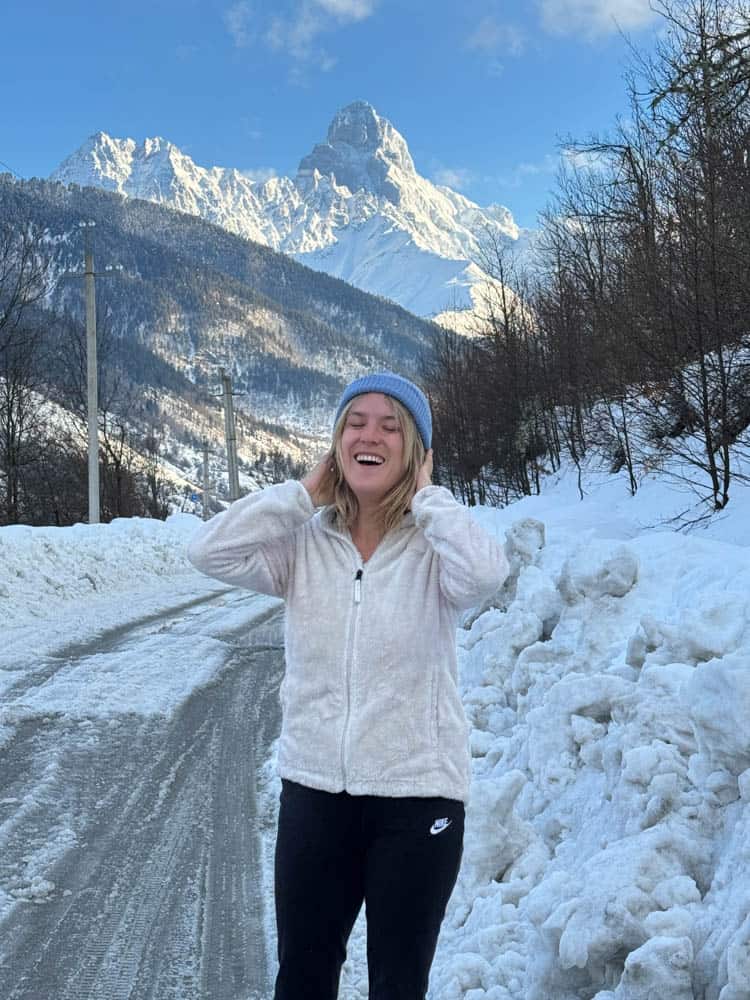 A woman standing on a snowy road with mountains in the background.