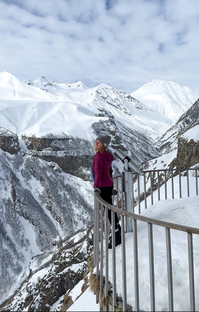 A woman standing on a railing overlooking snow covered mountains.