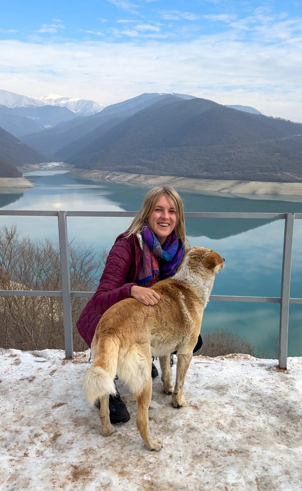A woman posing with her dog near a lake.